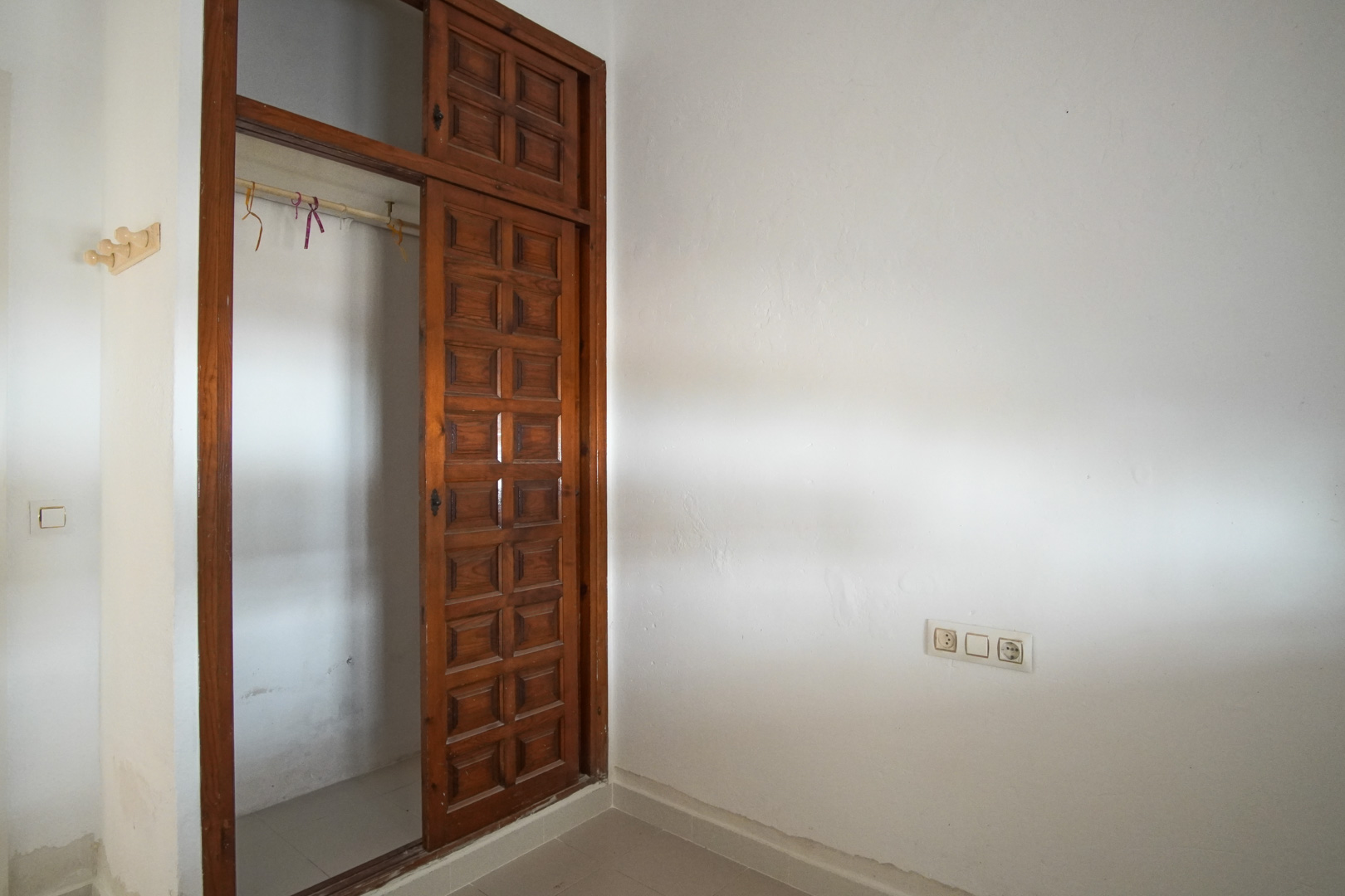 Bedroom featuring a built-in dark wood wardrobe with paneled sliding doors. The space includes textured white walls and integrated electrical outlets.