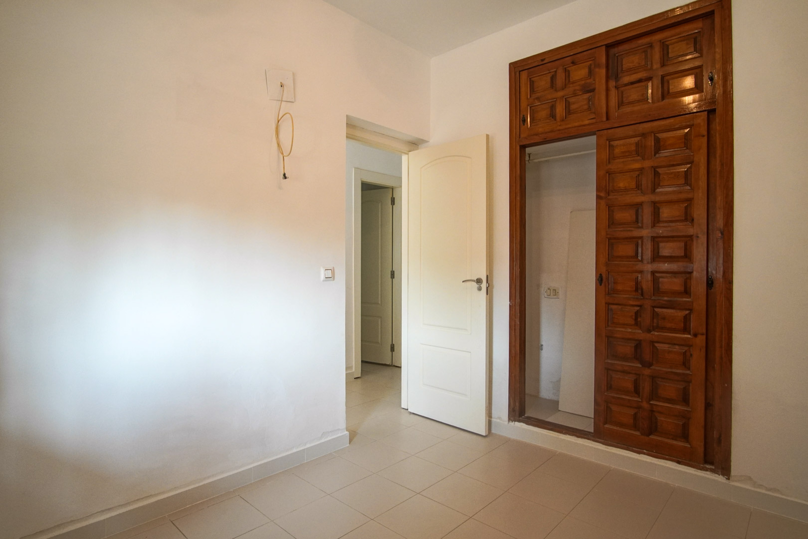 Bedroom featuring a built-in wardrobe with carved wood panels and tiled flooring. The space connects to the hallway and allows for personalized updates.
