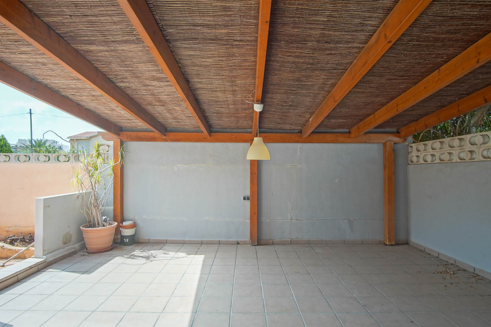 Covered outdoor terrace featuring a wooden beam structure with reed roofing, tiled flooring, and walls with decorative breeze blocks.