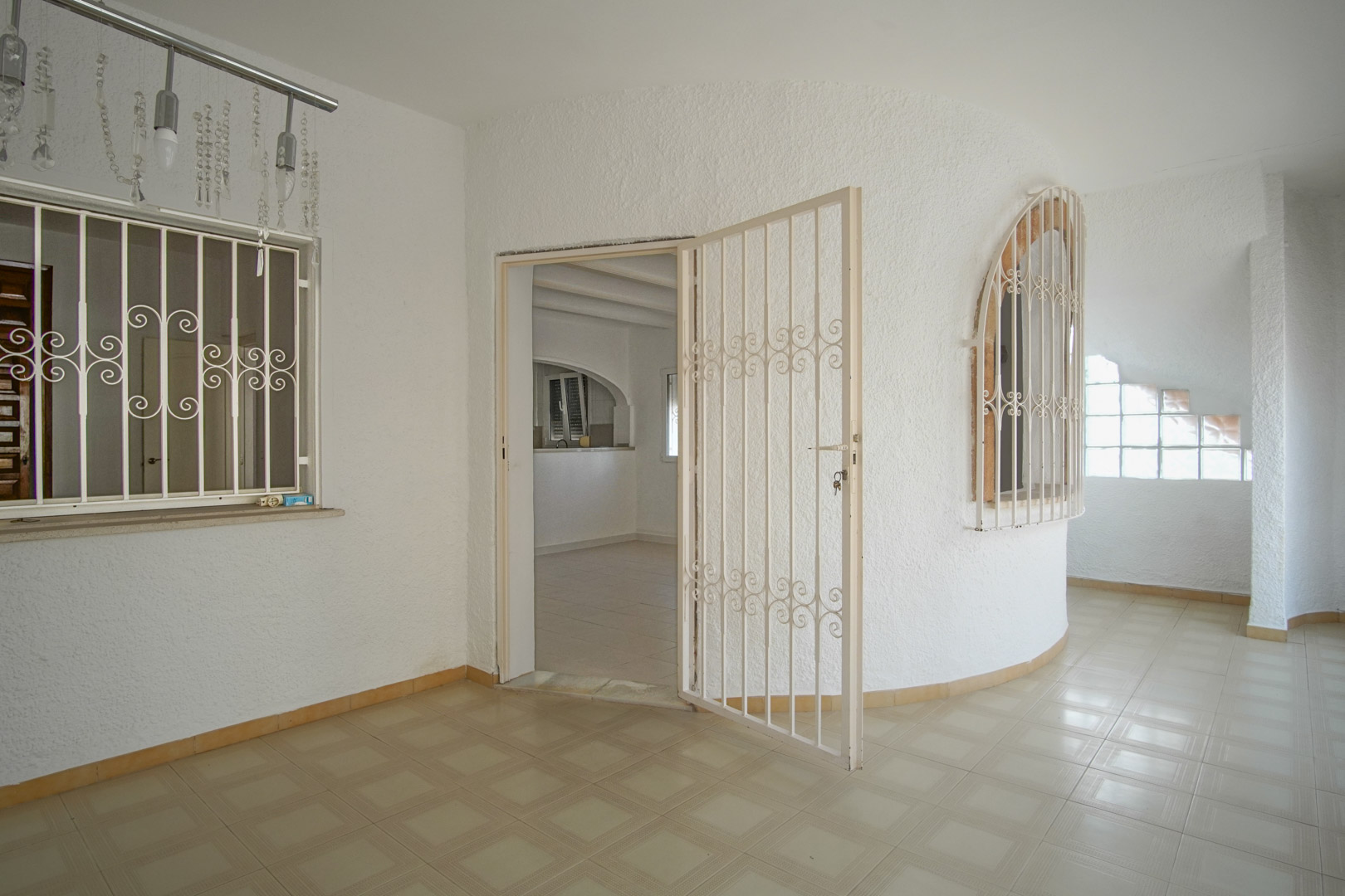 Covered terrace featuring patterned tile flooring, textured white walls, and decorative white security grilles on the arched windows and entrance.