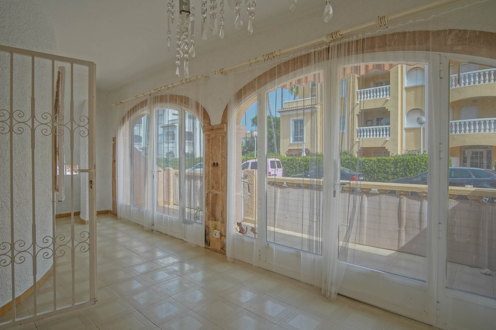 Enclosed terrace featuring large arched glass doors with natural stone pillars, light tiled flooring, and views of the residential surroundings.