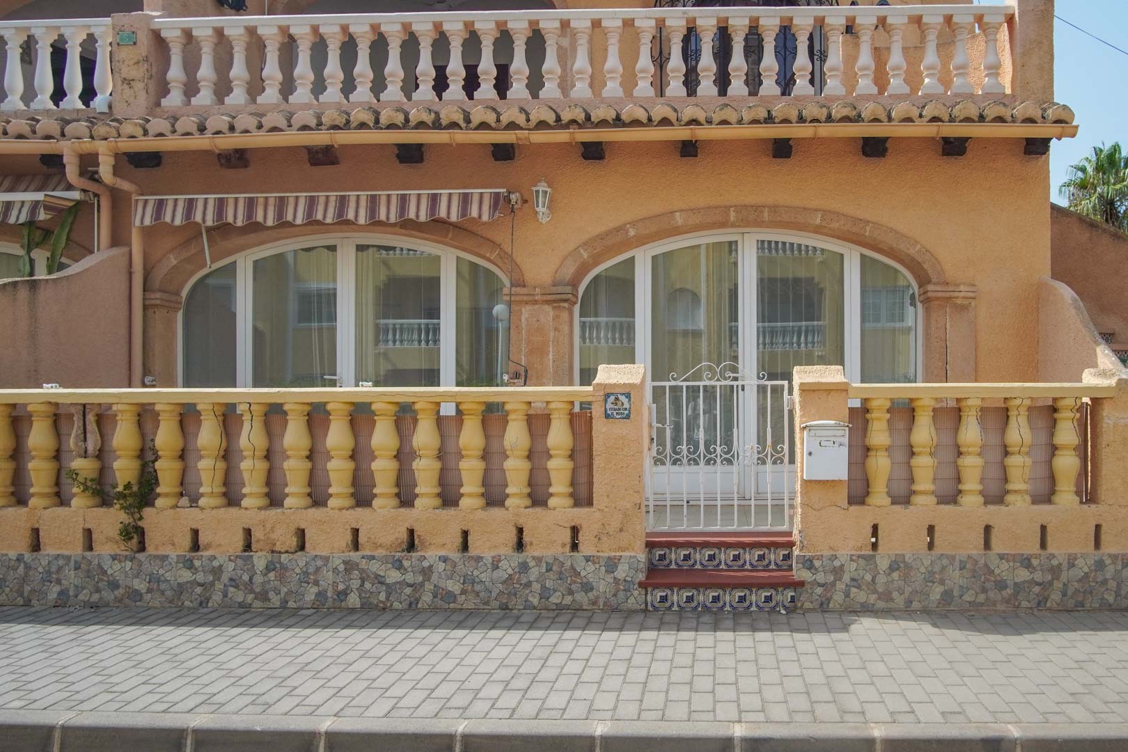 Ground floor exterior featuring a classic balustrade, white metal gate entry, and arched glass doors leading to the terrace area.
