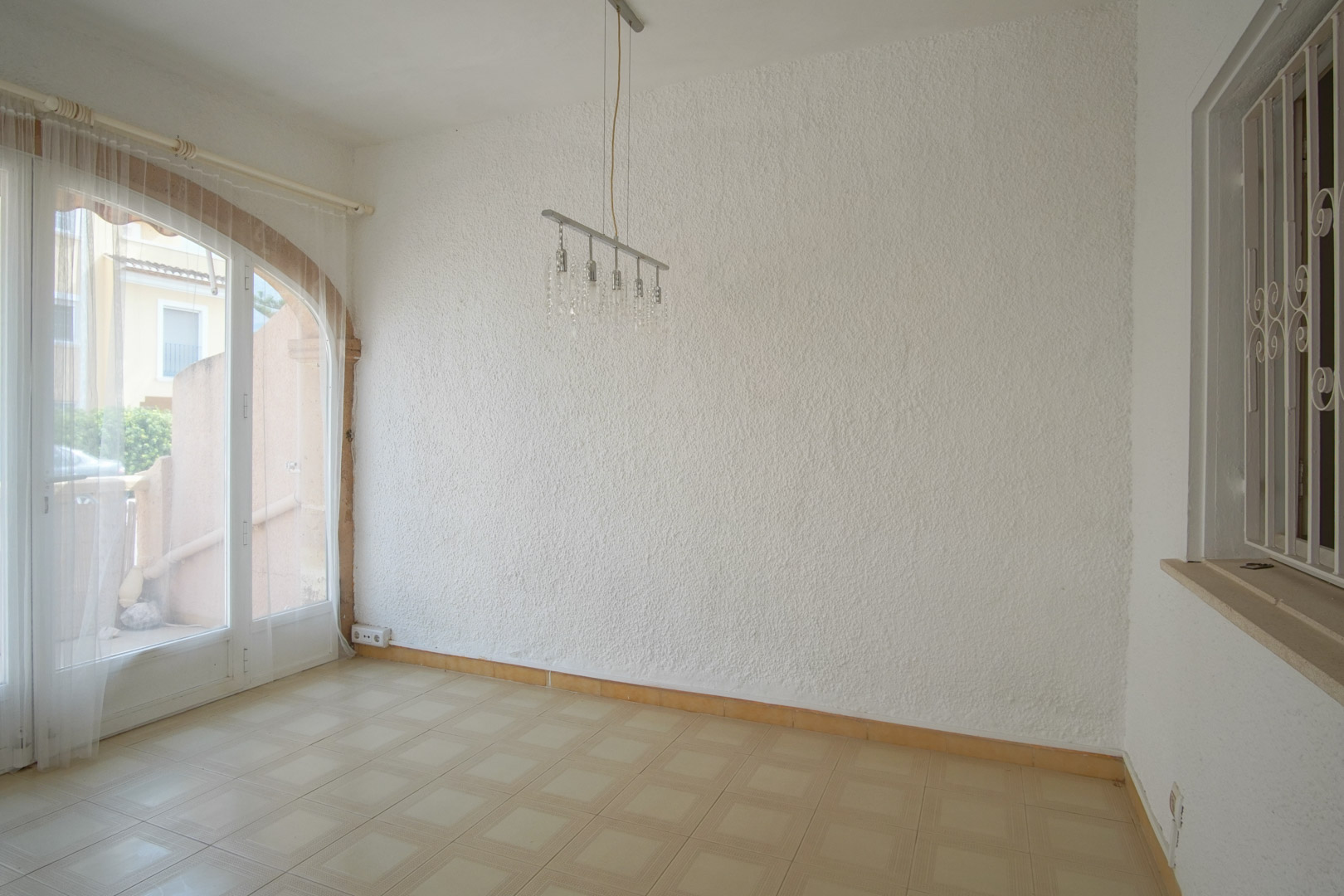 Living area featuring textured white walls, tiled flooring, and an arched glass door that provides direct access to the exterior.