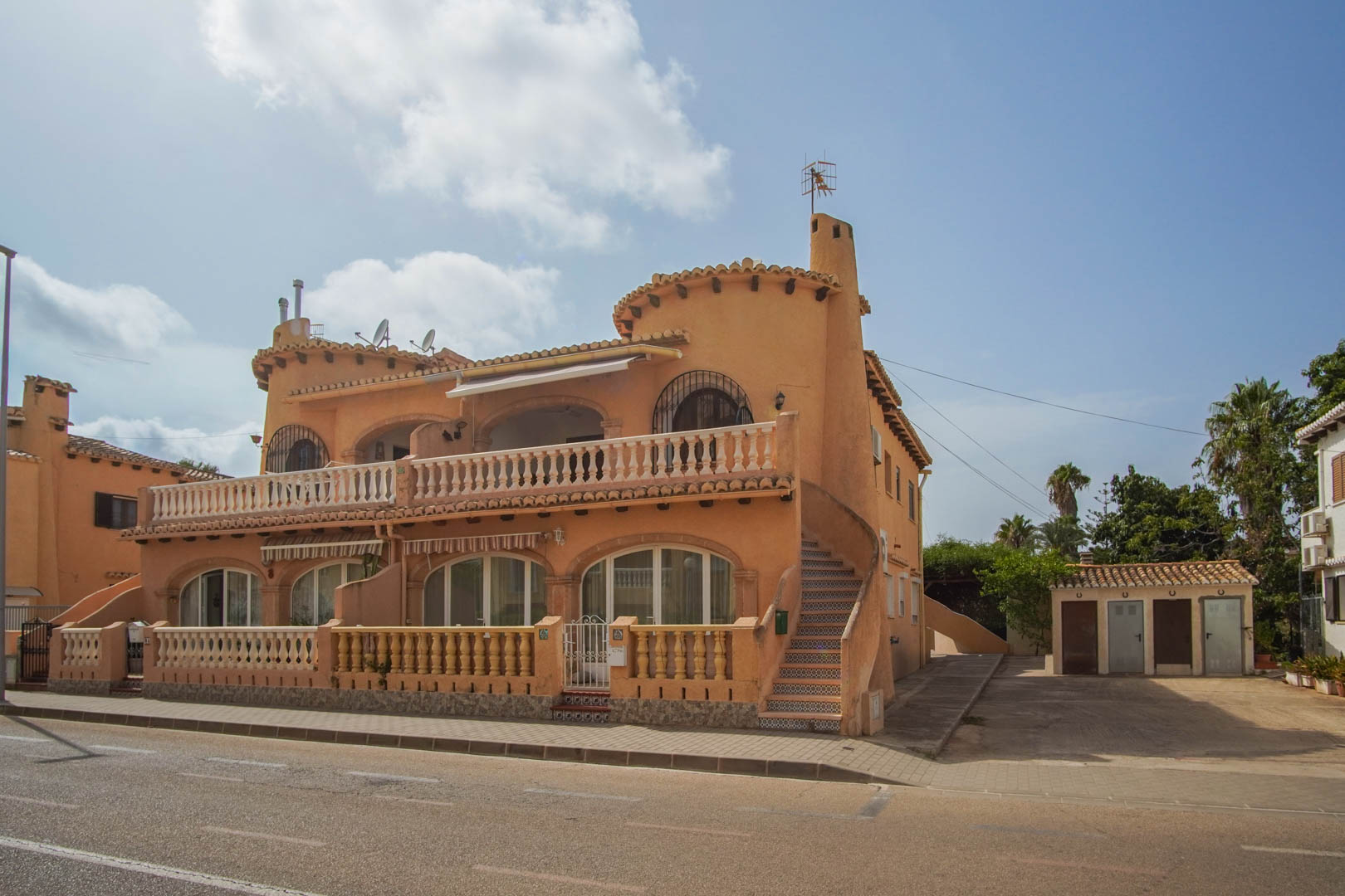 Mediterranean-style exterior featuring arched windows, stone balustrades, and a side staircase with decorative tiling, located at street level.