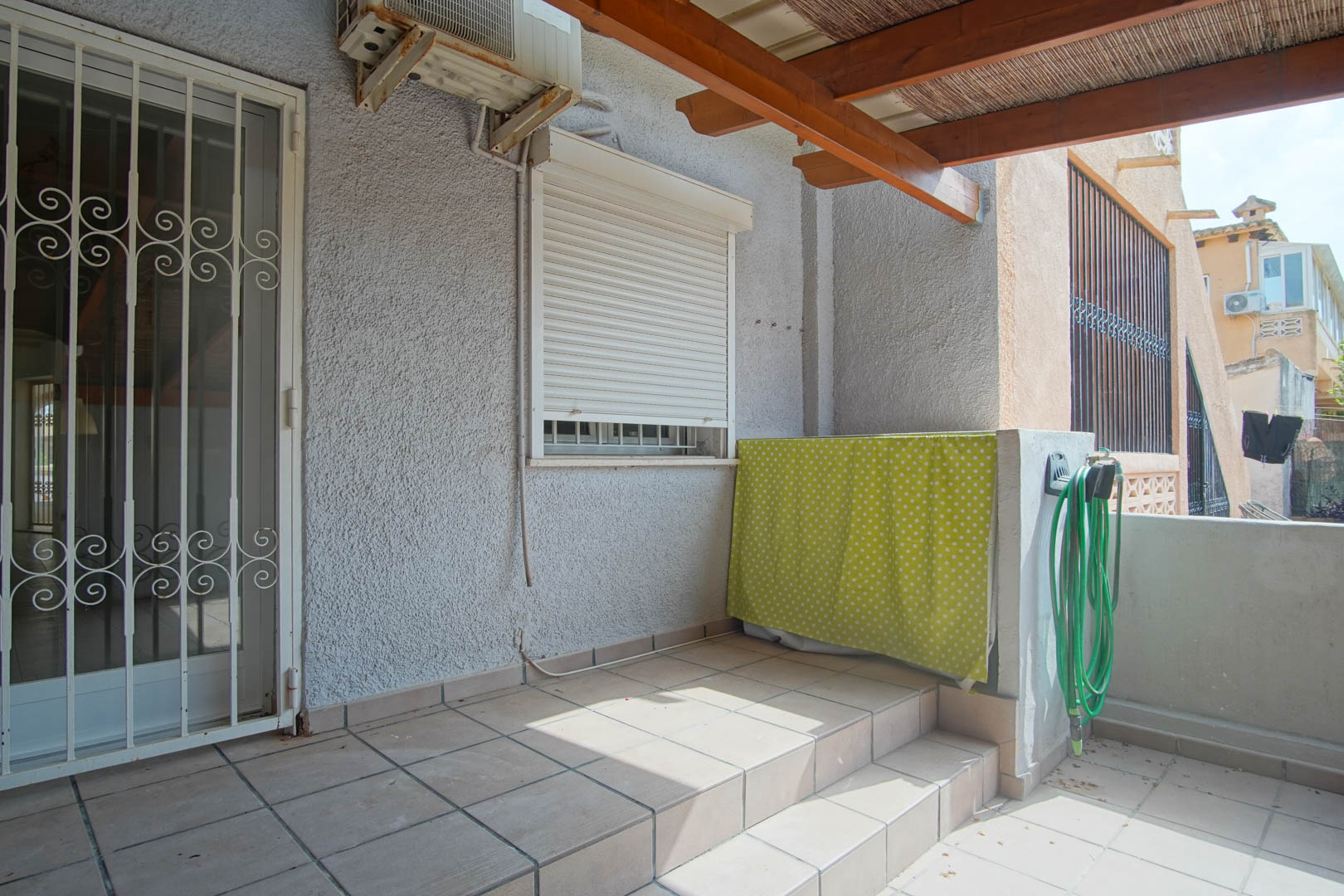 Outdoor terrace featuring ceramic tiling, a wooden pergola with reed shading, and a security gate. Equipped with an external AC unit and utility area.