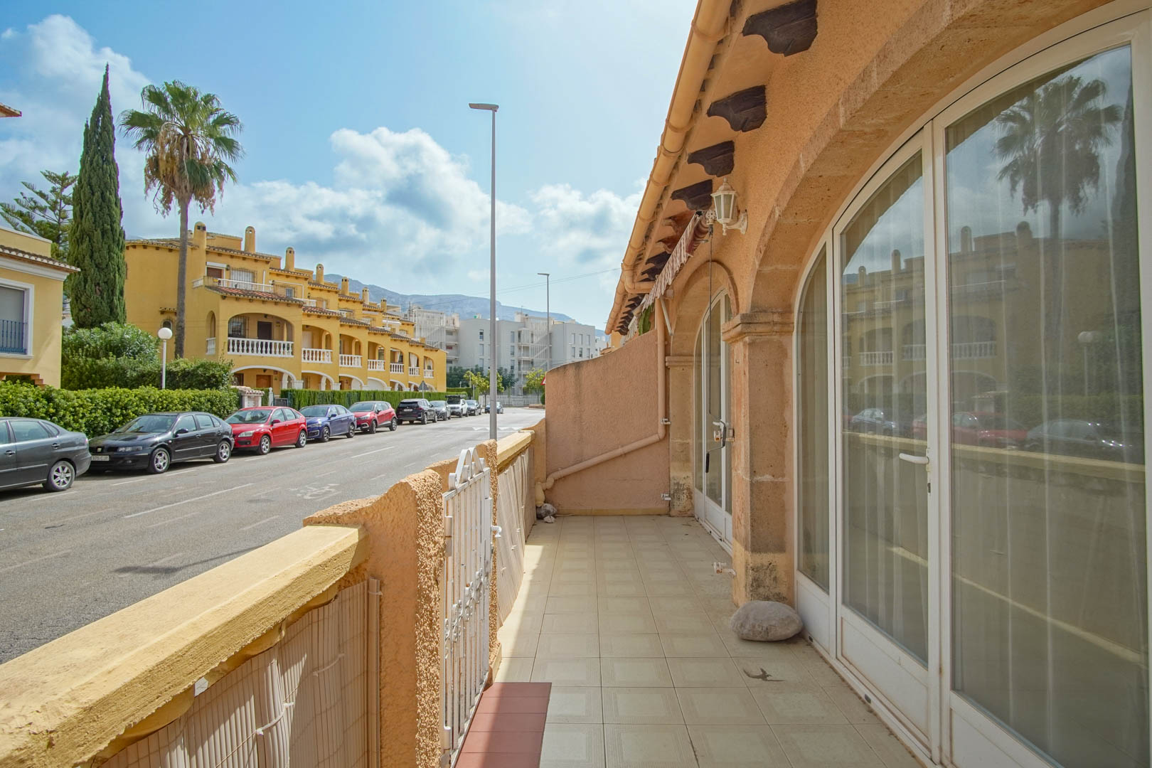 Outdoor terrace featuring ceramic tiling and large arched glass doors, offering a direct view of the residential street and surrounding Mediterranean architecture.