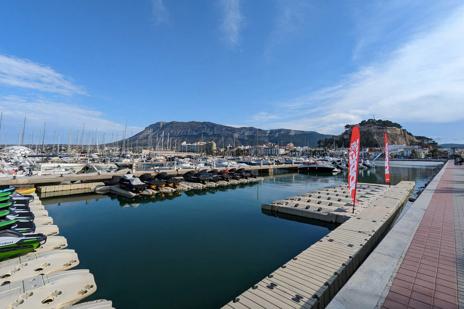 Panoramic views of Dénia's marina, featuring the historic castle and the Montgó mountain range in the background under a clear sky.