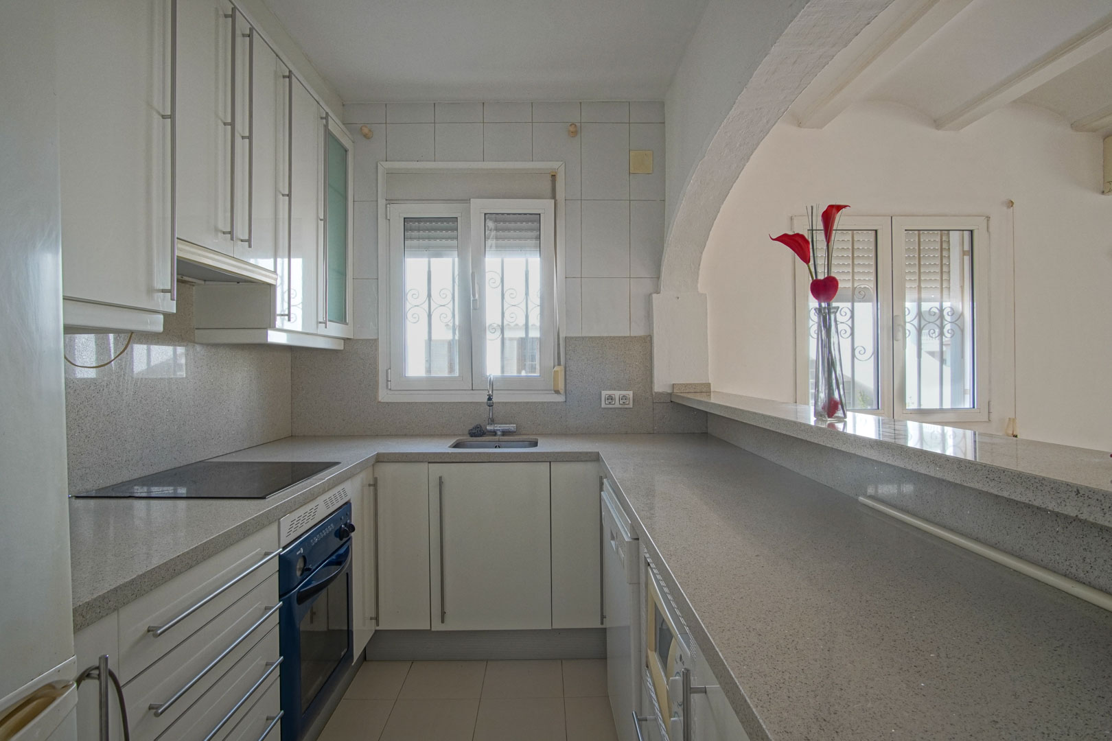 Semi-open kitchen featuring white cabinetry, grey granite countertops, and a breakfast bar connected to the living area via an arched opening.