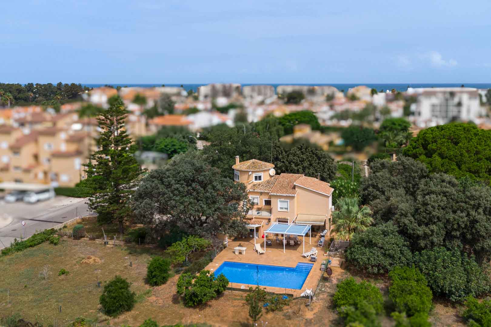 Aerial perspective of the Mediterranean villa showing the private pool, shaded terraces, and expansive flat plot surrounded by mature trees near the sea.