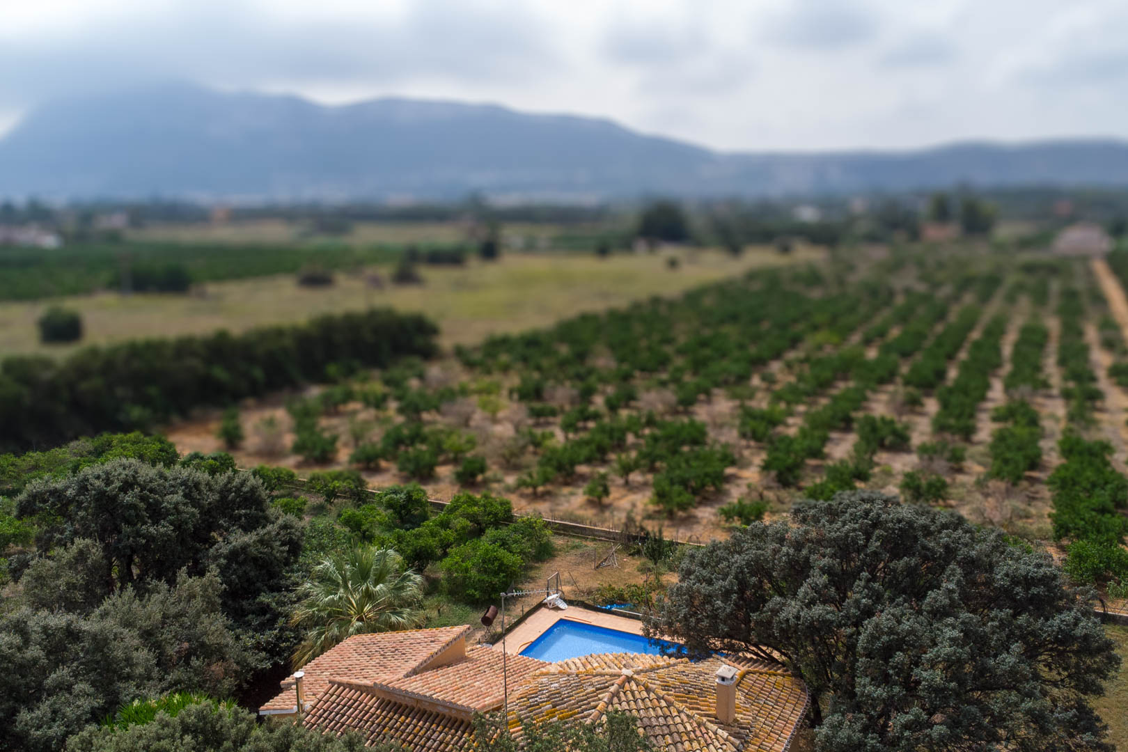 Aerial view featuring the private swimming pool and tiled roof, set against a backdrop of agricultural fields and distant mountain silhouettes.