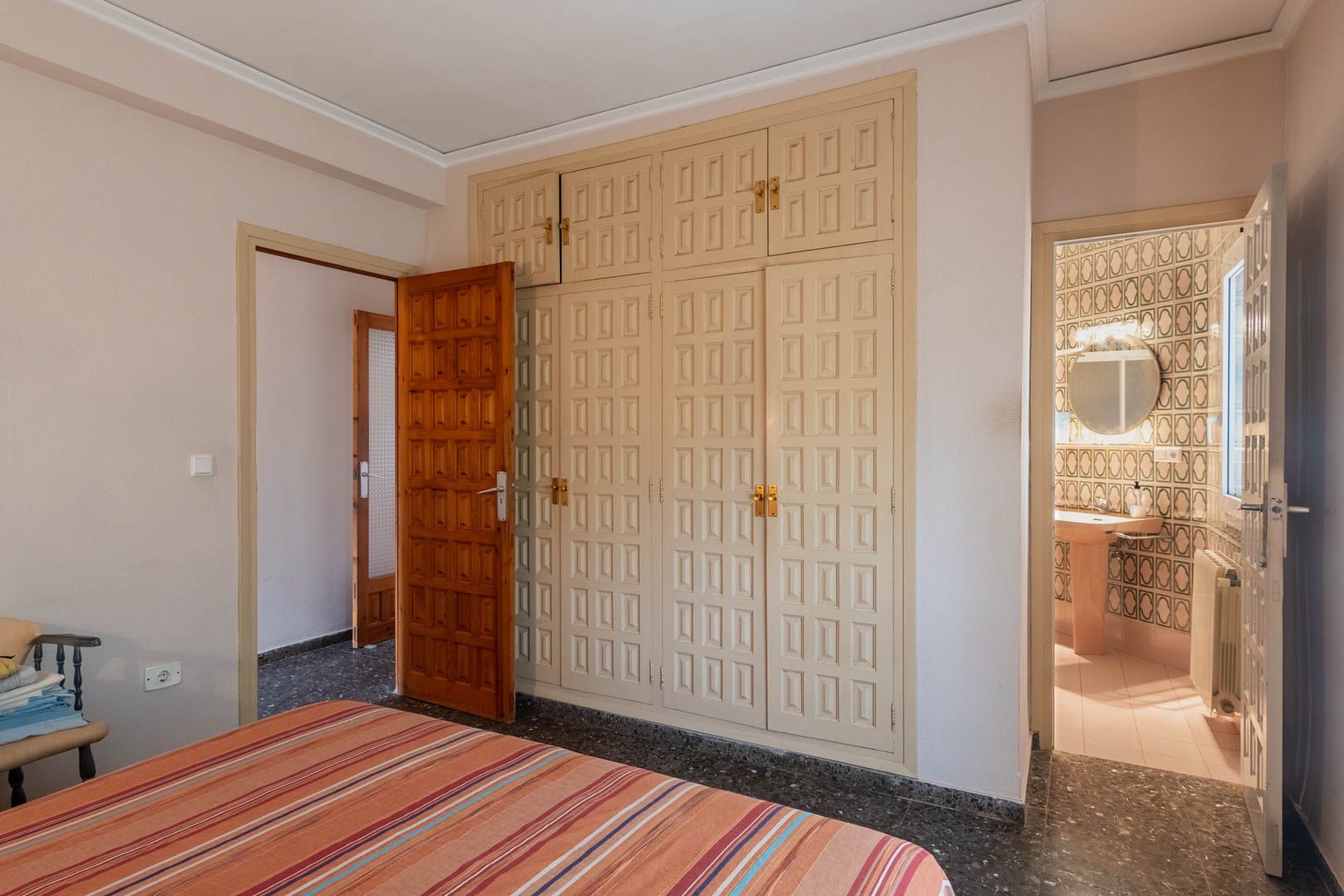 Bedroom featuring a large built-in wardrobe with paneled doors and an en-suite bathroom with vintage geometric tiling and natural light.