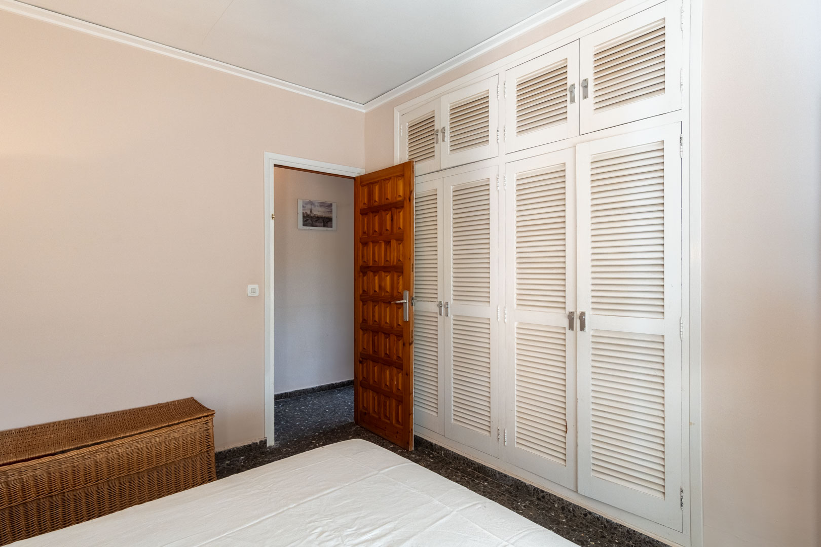 Bedroom featuring a large built-in wardrobe with white louvered doors, dark terrazzo flooring, and a traditional solid wood paneled door.