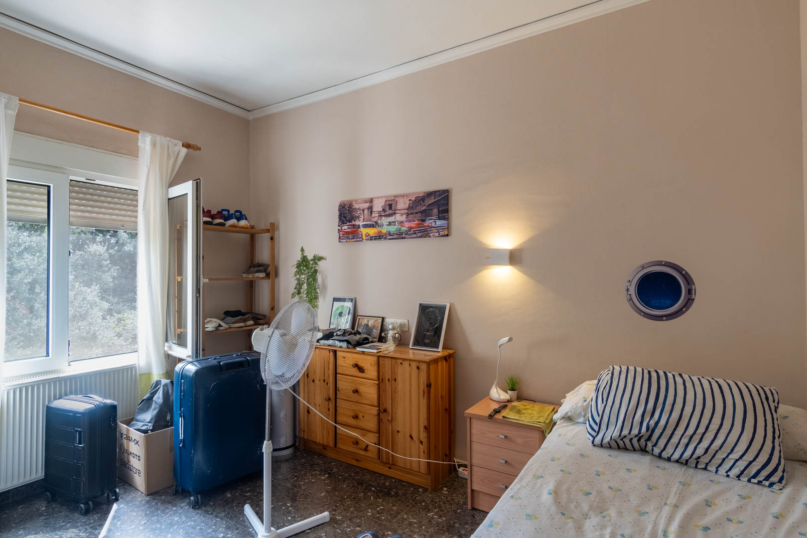 Bedroom featuring terrazzo flooring, natural wood furniture, and an exterior window. Equipped with a radiator and warm wall-mounted lighting.