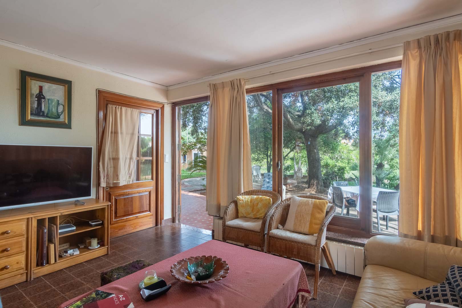 Bright living area featuring ceramic tile flooring, wooden cabinetry, and large timber-framed windows overlooking the leafy garden and outdoor terrace.