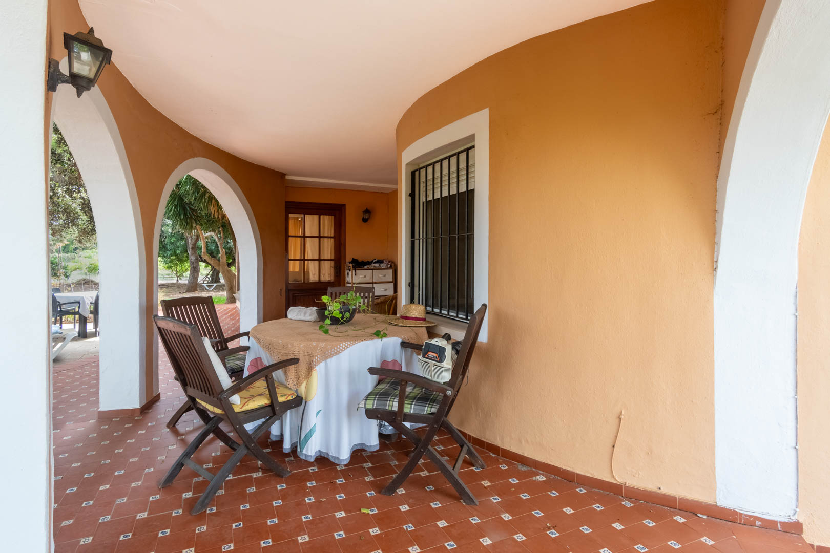 Covered porch featuring classic Mediterranean arches and terracotta tile flooring. This shaded outdoor dining area offers direct access to the garden.