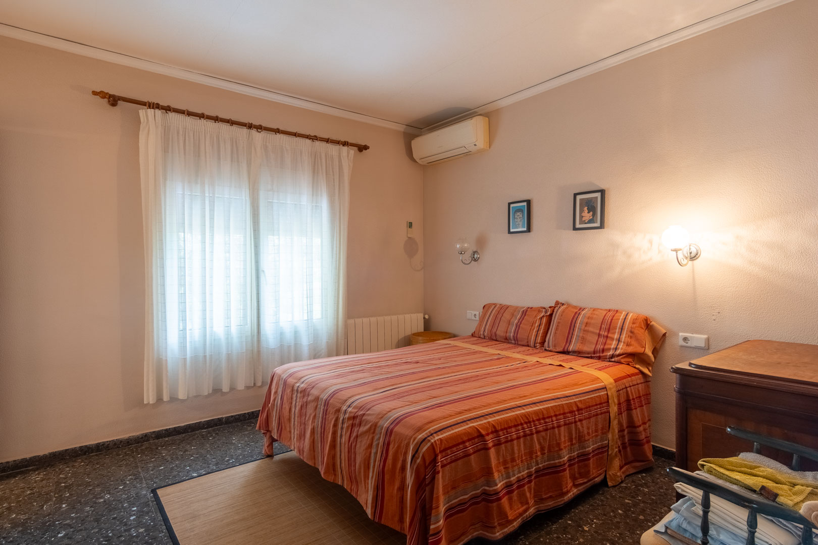 Double bedroom featuring dark terrazzo flooring, wall-mounted air conditioning, a radiator, and a window with white curtains for soft natural light.