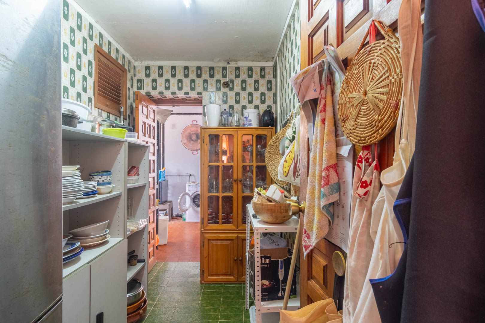 Functional pantry with vintage patterned tiles, open shelving for crockery, and a wooden display cabinet, leading to the laundry room.