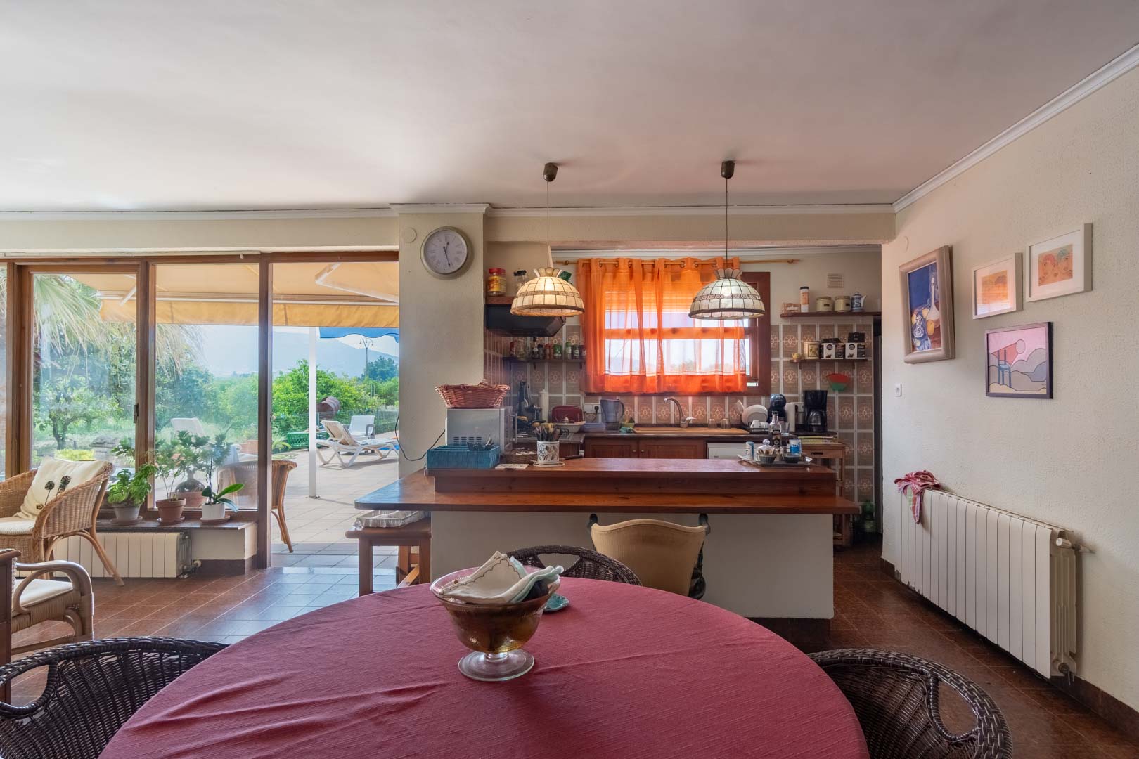 Open-plan kitchen featuring a wooden breakfast bar and dining area, with large sliding glass doors opening onto a sun-drenched terrace and garden.