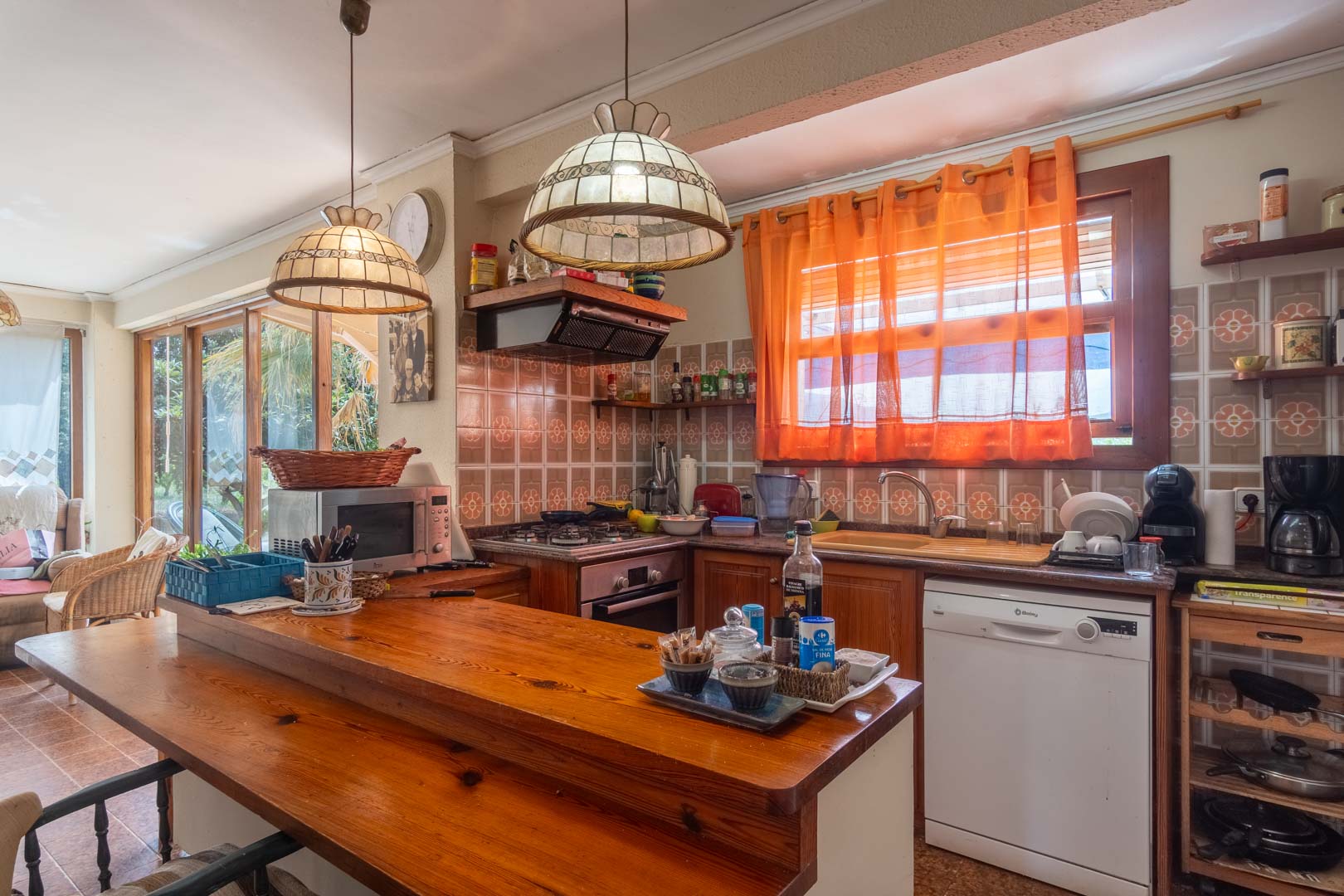 Rustic kitchen featuring a solid wood breakfast bar, traditional floral tiles, and decorative pendant lighting. The space includes integrated appliances.