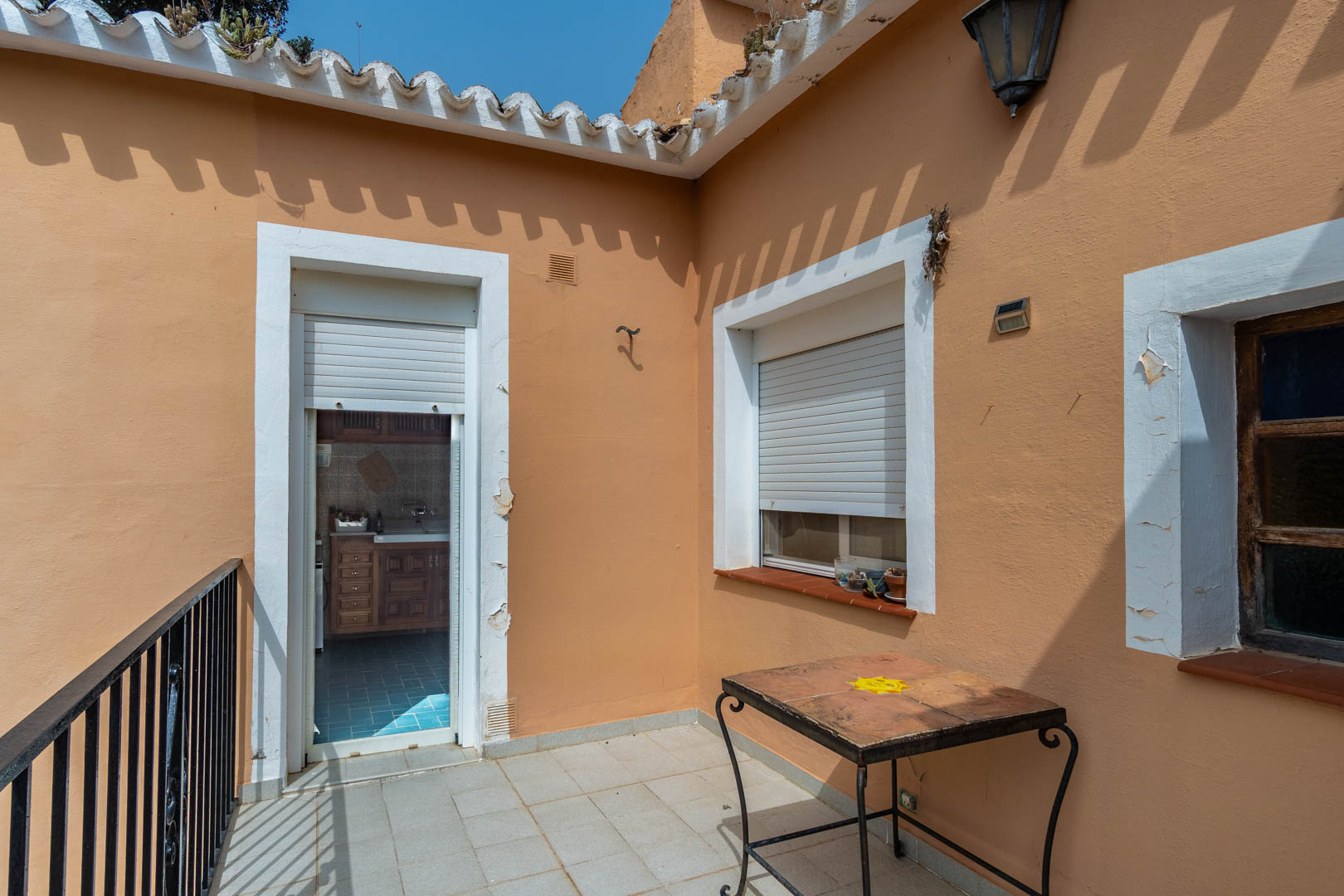Upper terrace with tiled flooring and wrought iron railings, offering direct access to the independent kitchen through a doorway with rolling shutters.