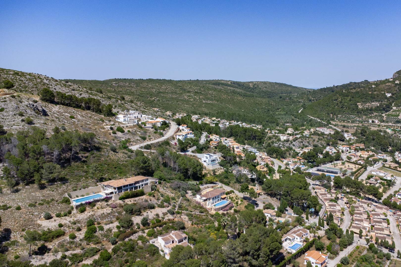 Aerial view of the elevated residential area in Alcalalí, showcasing villas integrated into the hillside of the Jalón Valley amidst Mediterranean landscape.