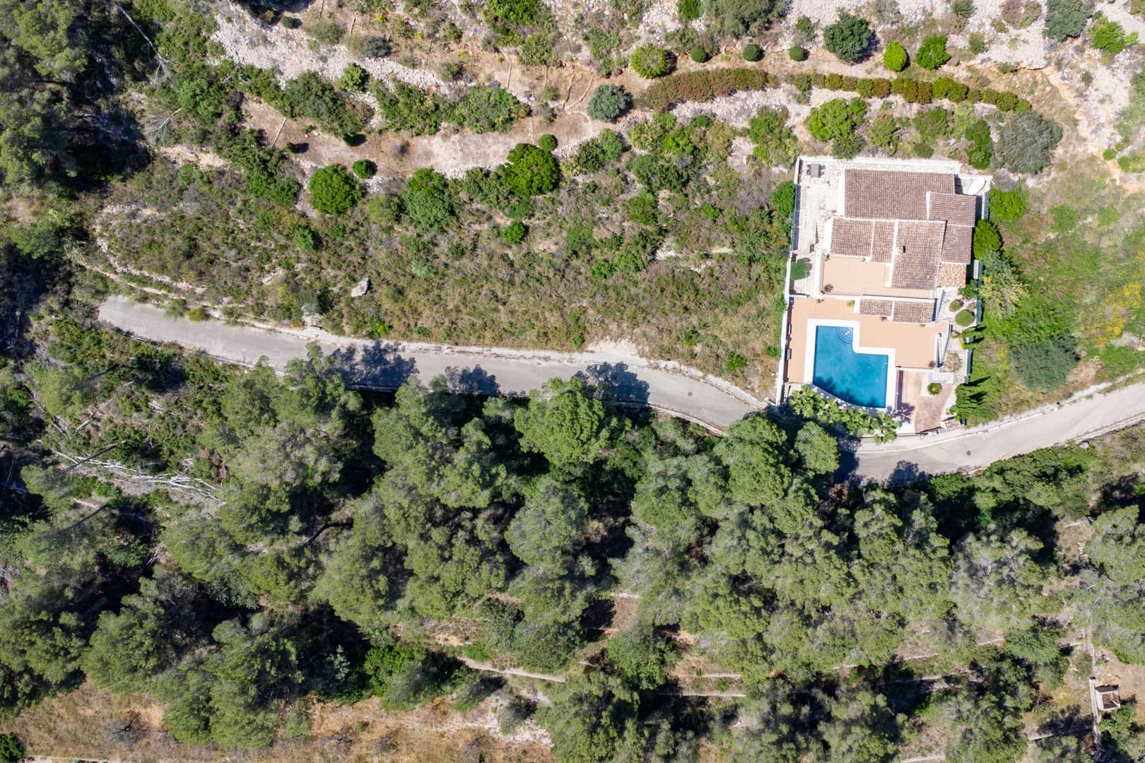 Overhead aerial view of a villa featuring a private pool, terracotta roof, and terraced grounds nestled within a dense Mediterranean pine forest.