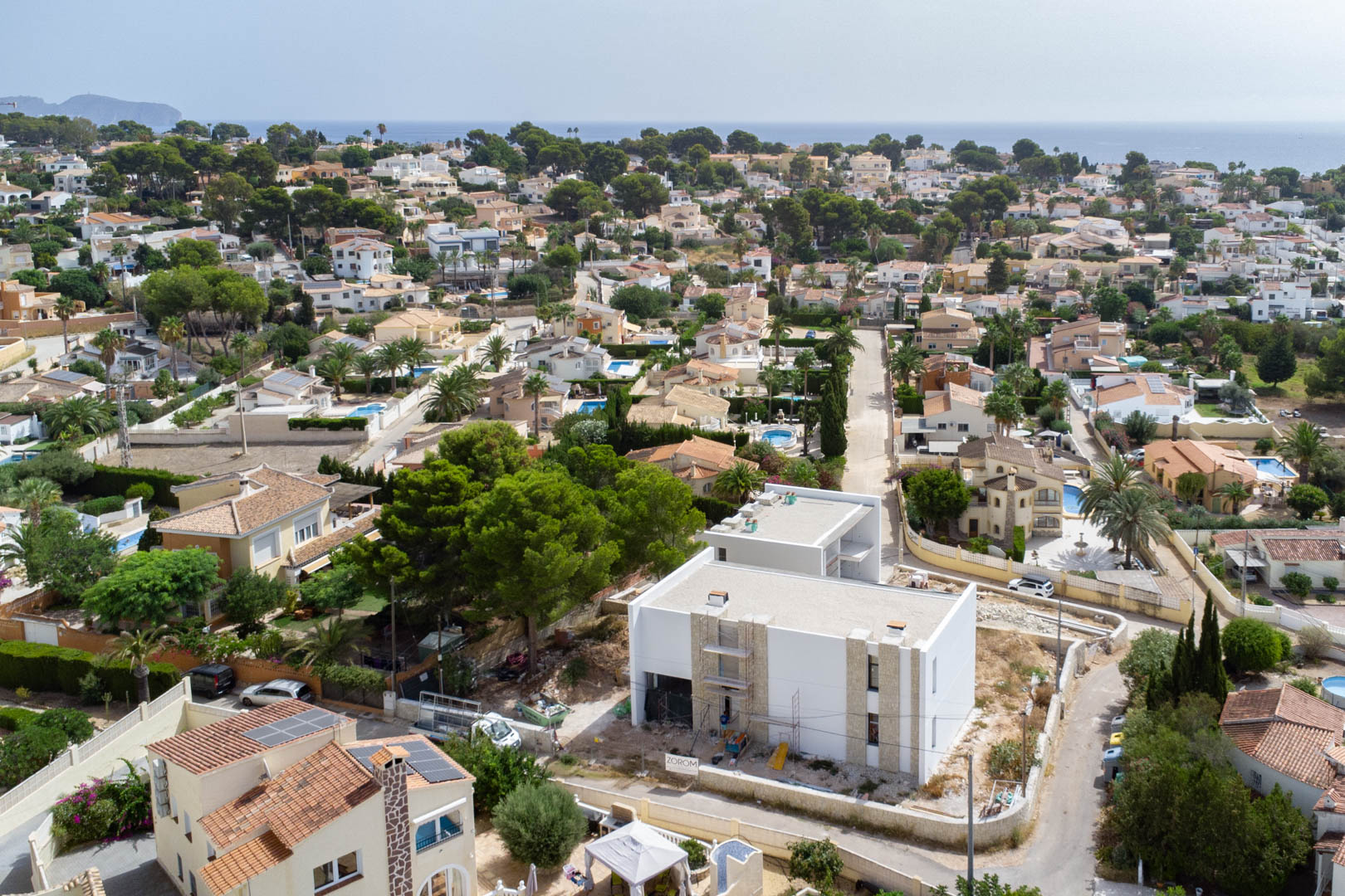 Aerial perspective of the villa under construction, showcasing the white exterior with stone cladding in a residential neighborhood with sea views.