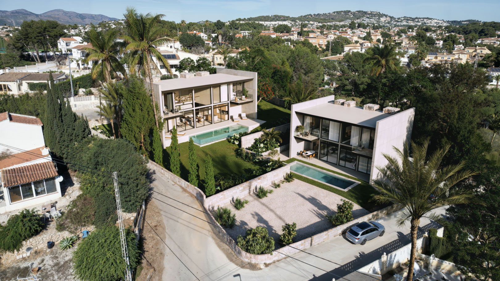 Aerial perspective of two contemporary villas featuring glass walls, rectangular pools, and landscaped gardens with palms in Calpe's La Merced area.