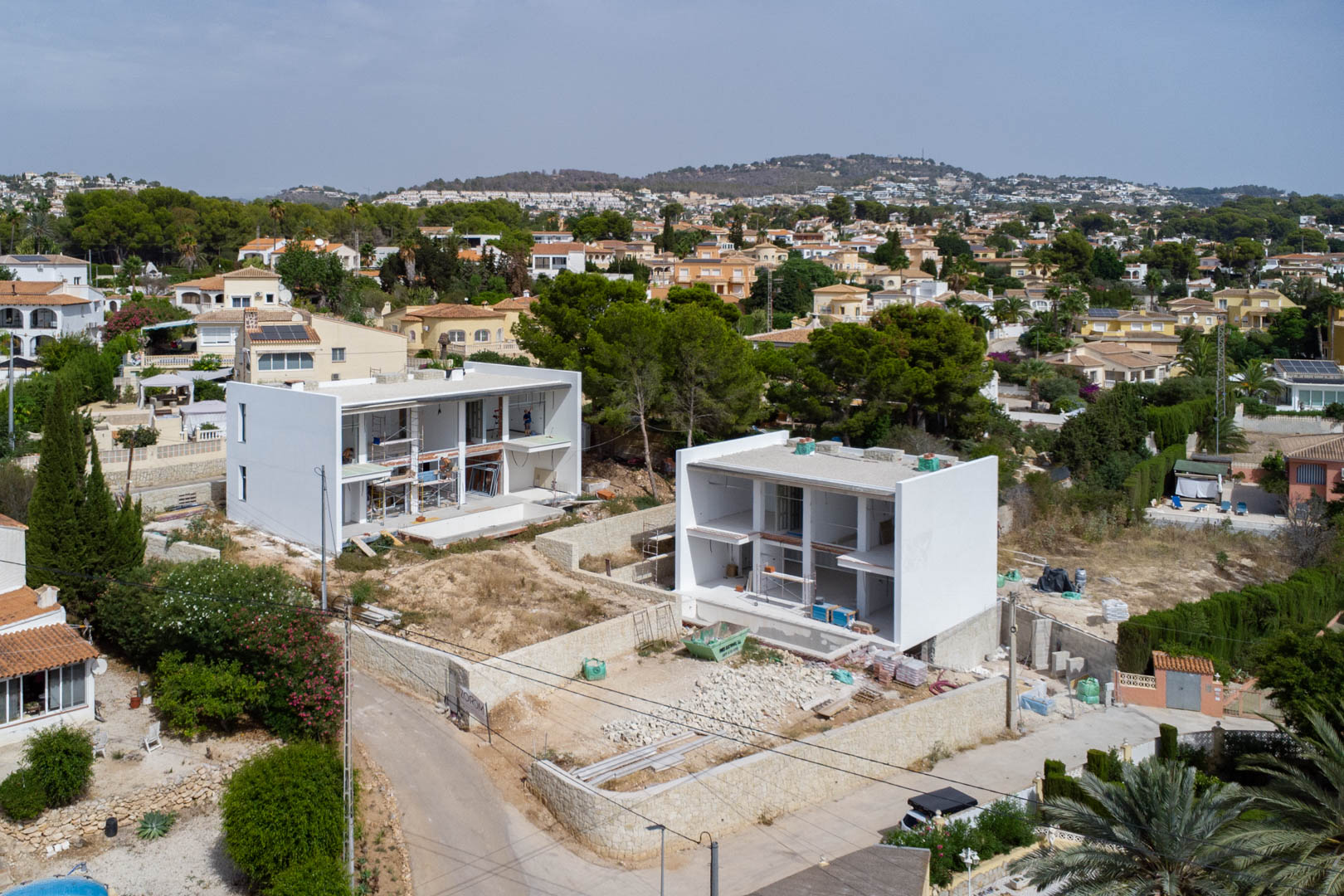 Aerial view of the construction phase of two modern villas in Calpe, showcasing the white structures, natural stone walls, and plot leveling.