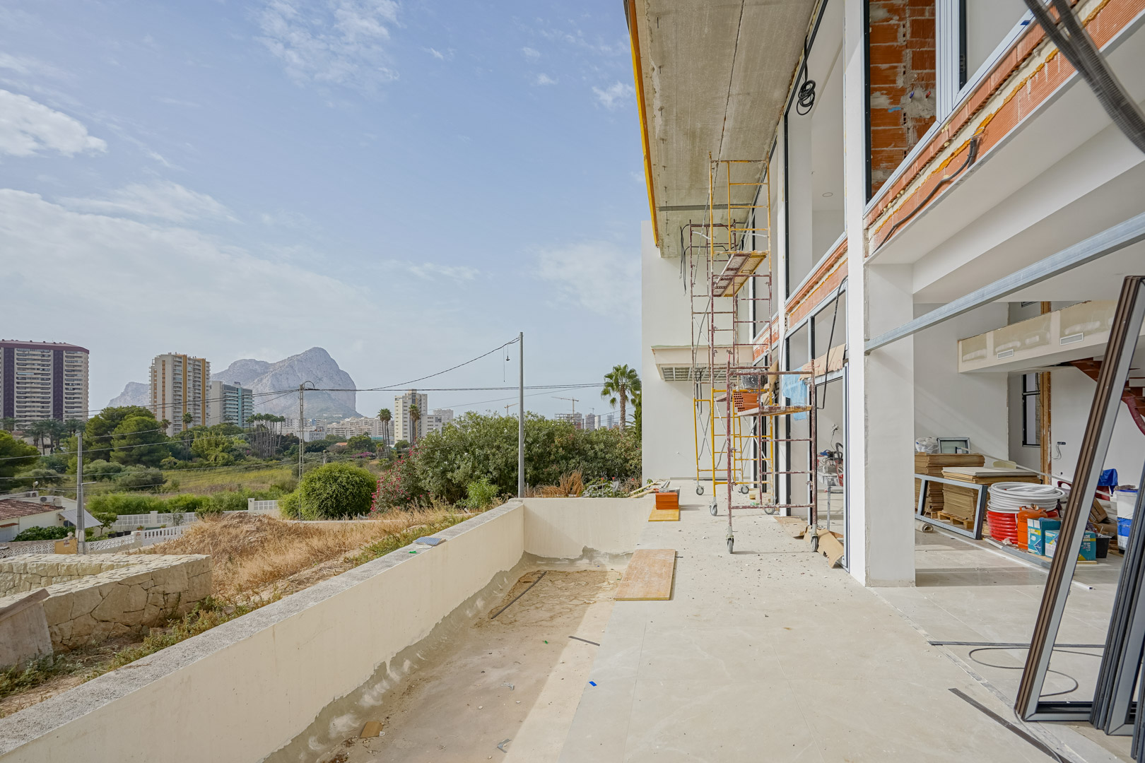 Exterior view of the villa under construction featuring scaffolding, large window openings, and a terrace overlooking the Peñón de Ifach in Calpe.