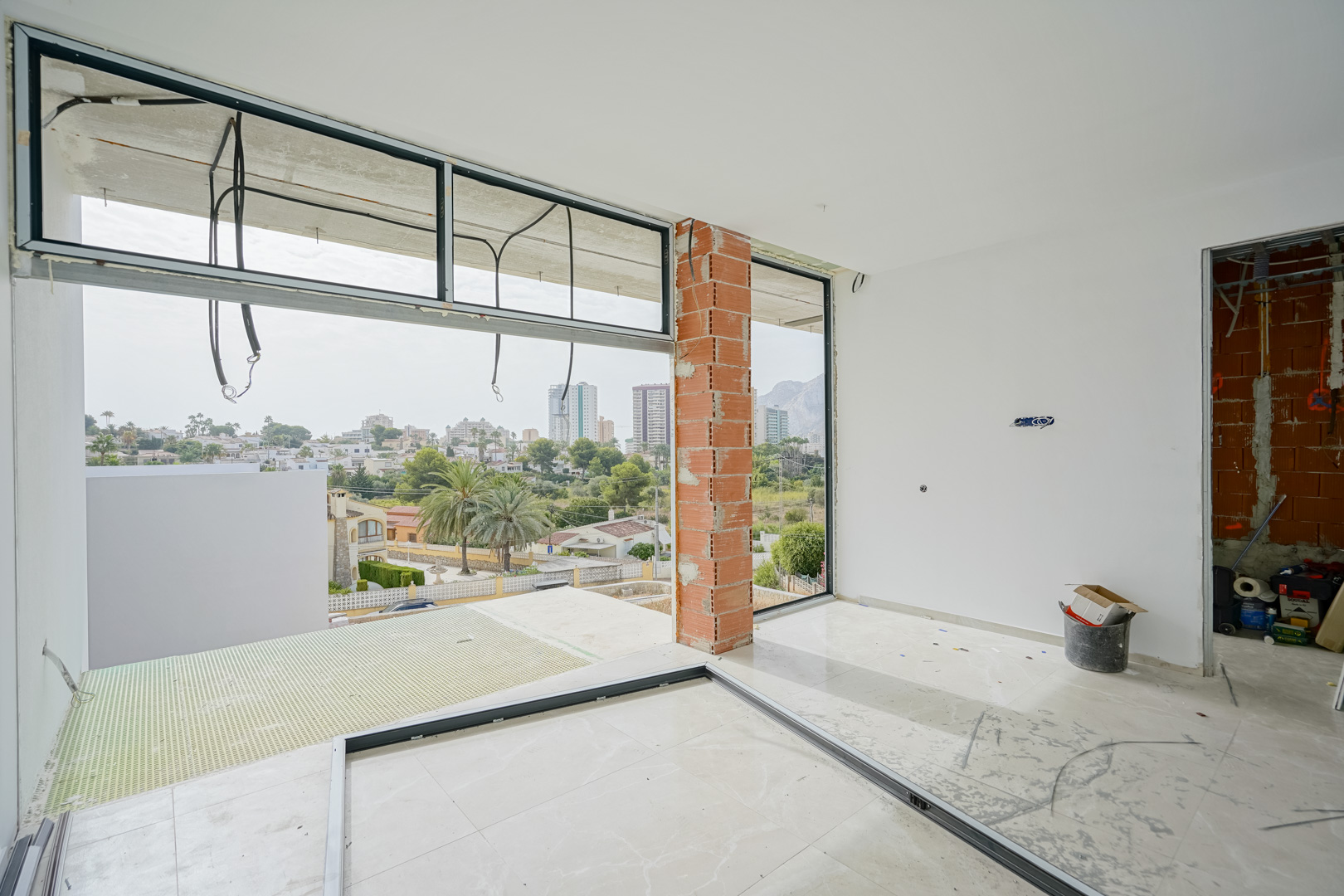 Interior view of the villa under construction, showing large window frames and panoramic views of the Peñón de Ifach and Calpe skyline.