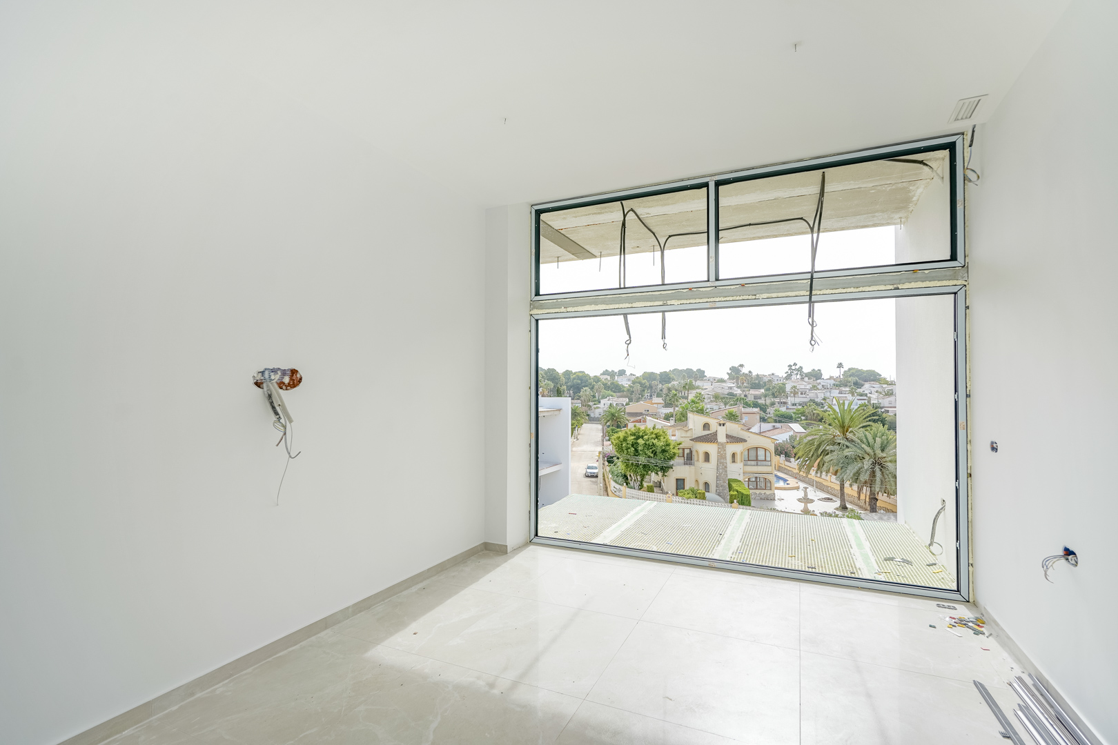 Room under construction featuring floor-to-ceiling windows, light porcelain tile flooring, and open views of the surrounding residential area in Calpe.