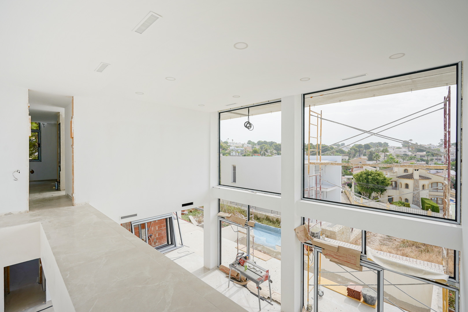 Upper floor perspective of the double-height living room featuring expansive windows, recessed ceiling lights, and integrated air conditioning vents.