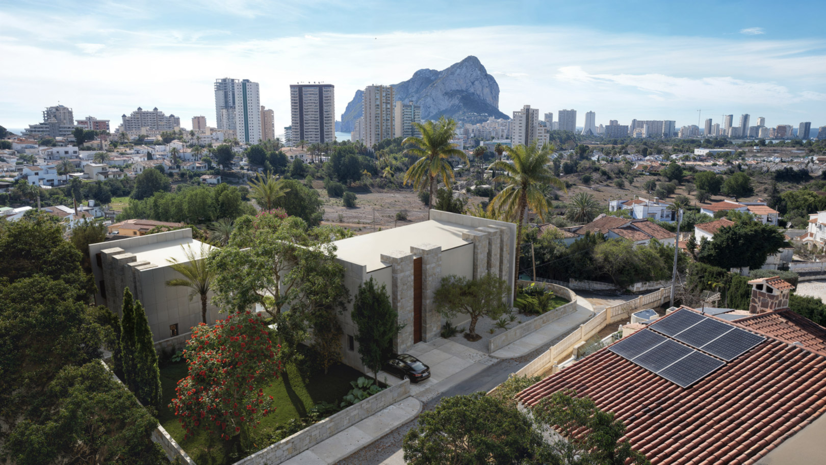Aerial view of the modern villa featuring natural stone facades and landscaped gardens, with the iconic Peñón de Ifach visible in the Calpe skyline.