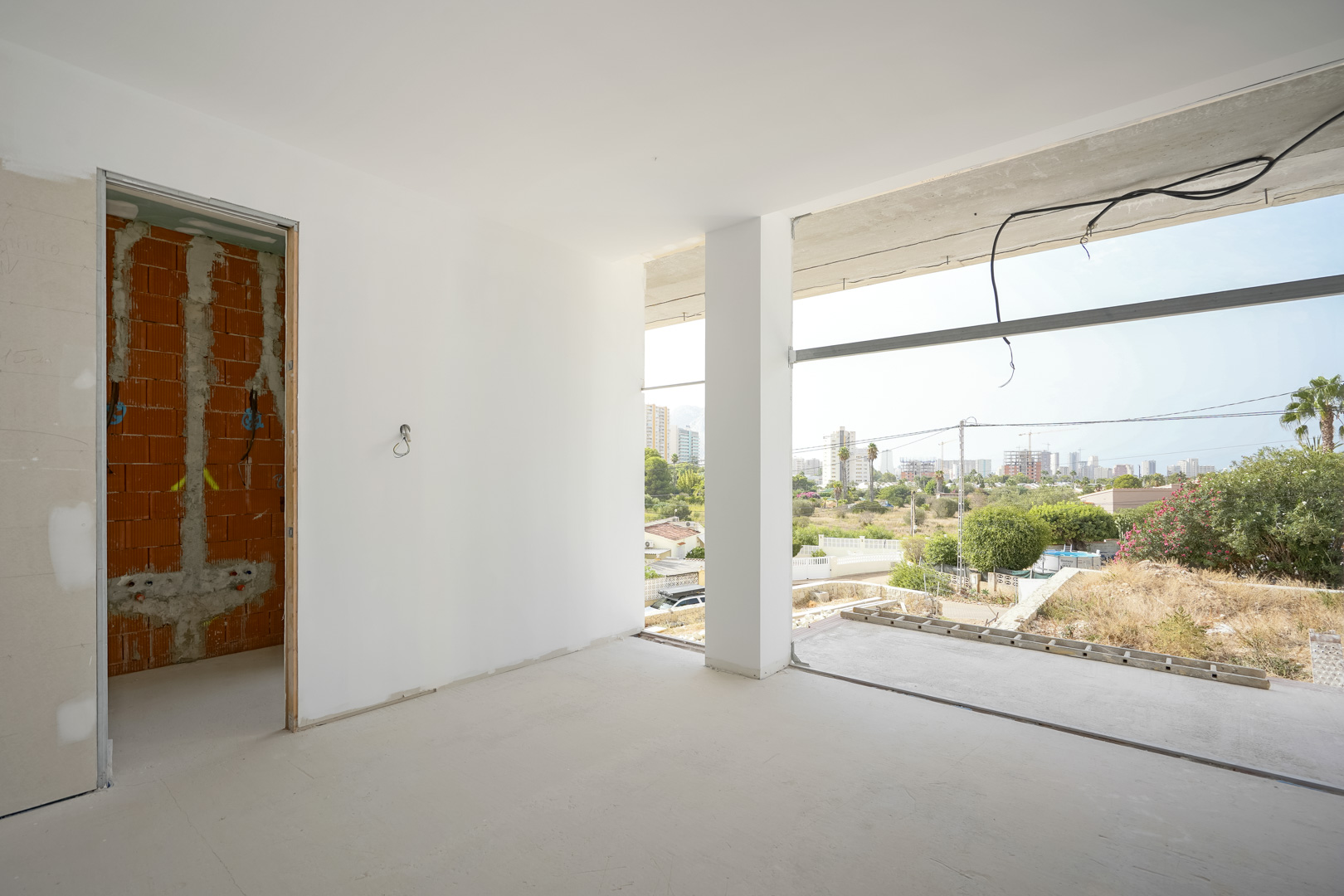 Interior view of a room under construction featuring large floor-to-ceiling openings with views of the Calpe skyline and the Peñón de Ifach.