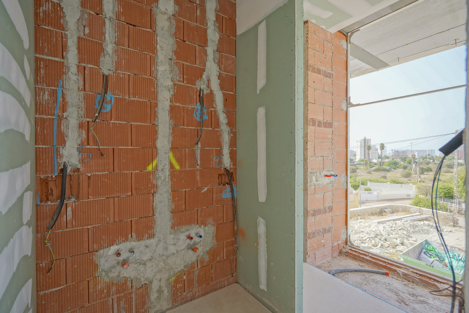 Interior view of the construction progress showing ceramic brick walls, electrical conduits, and plumbing rough-ins next to a large window opening.