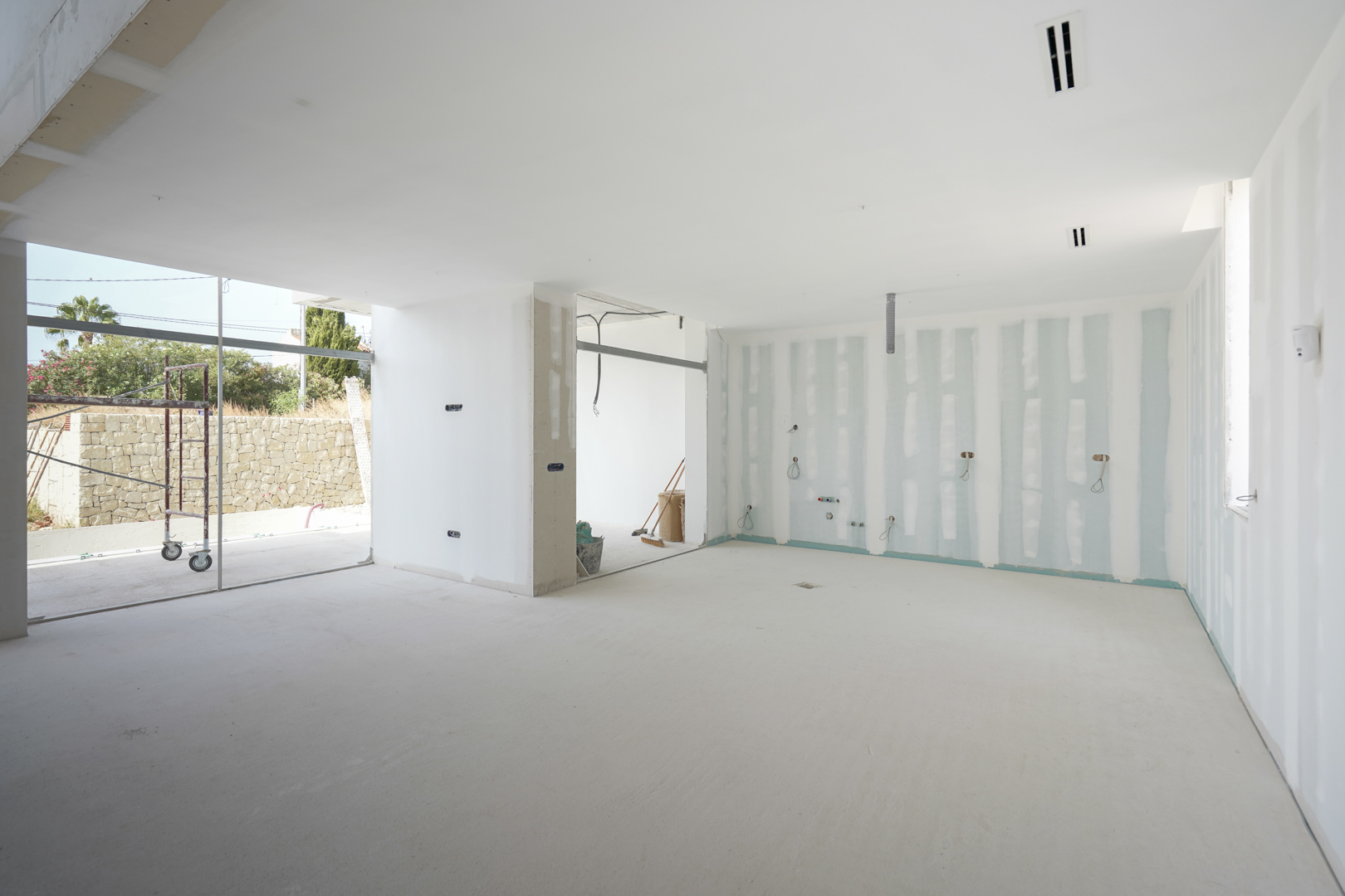 Interior view of the open-plan living area under construction, featuring recessed ceiling vents and large floor-to-ceiling window frames.
