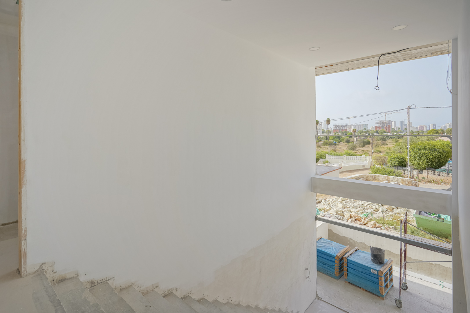 View from the unfinished staircase showing the large window opening, recessed ceiling lighting, and the surrounding Calpe skyline during construction.
