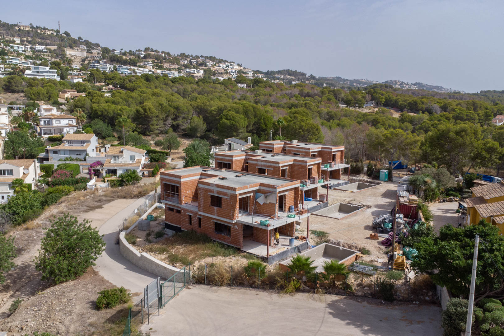 Aerial perspective of the construction site for three luxury villas, showcasing the structural brickwork and private pool basins integrated into the natural landscape.
