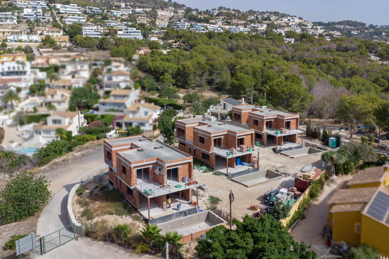 Aerial view of the three luxury villas during the structural construction phase, featuring brickwork shells and private pool excavations on individual plots.
