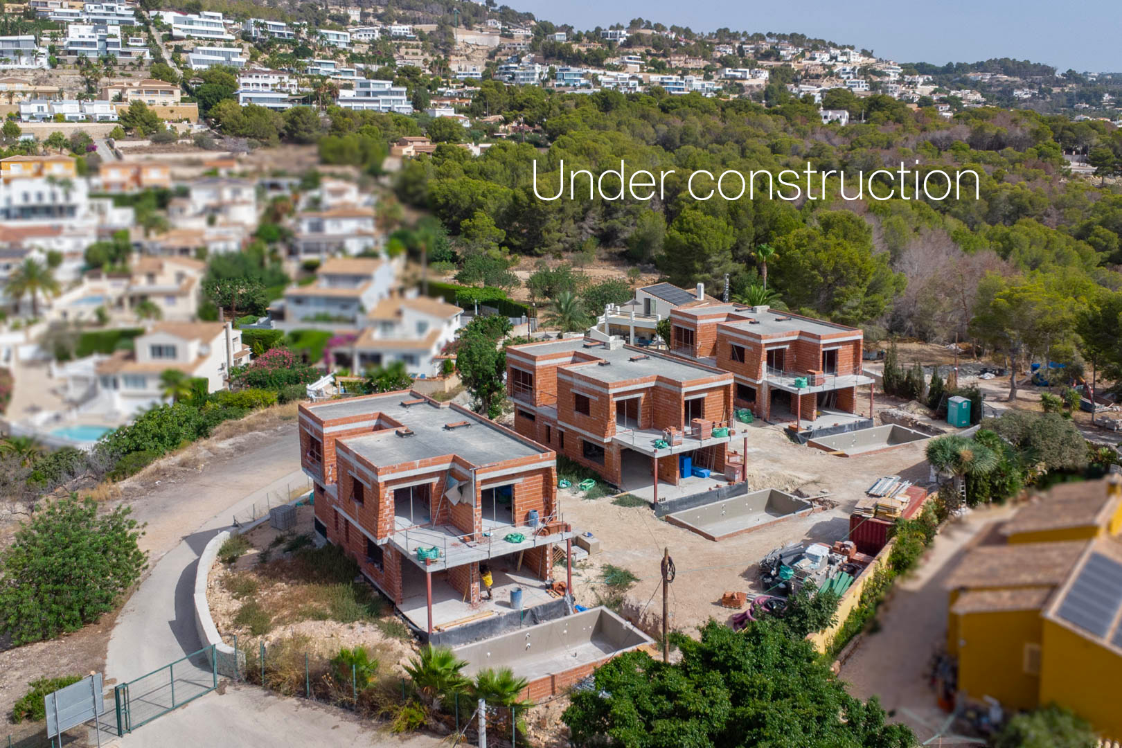 Aerial view of the three villas under construction in Calpe, featuring brick structures, concrete slabs, and excavated pool areas in a quiet residential setting.