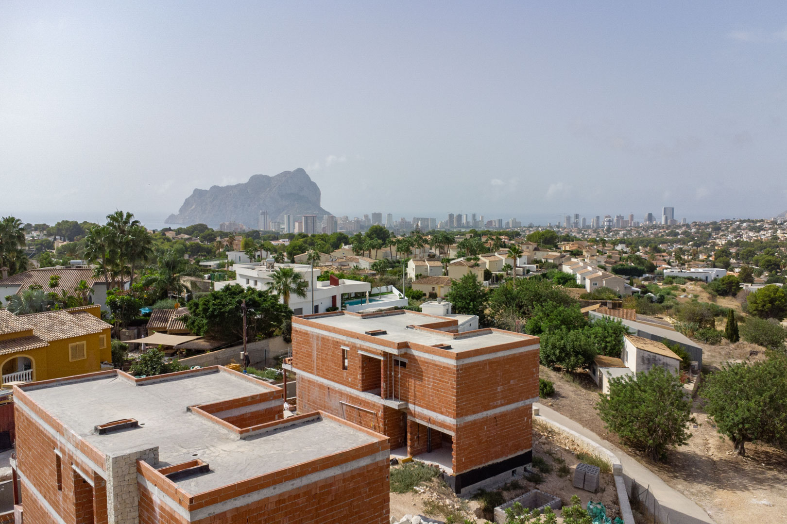 Aerial view showing the brick structure of the villas under construction, featuring panoramic views of the Peñón de Ifach and the Calpe skyline.