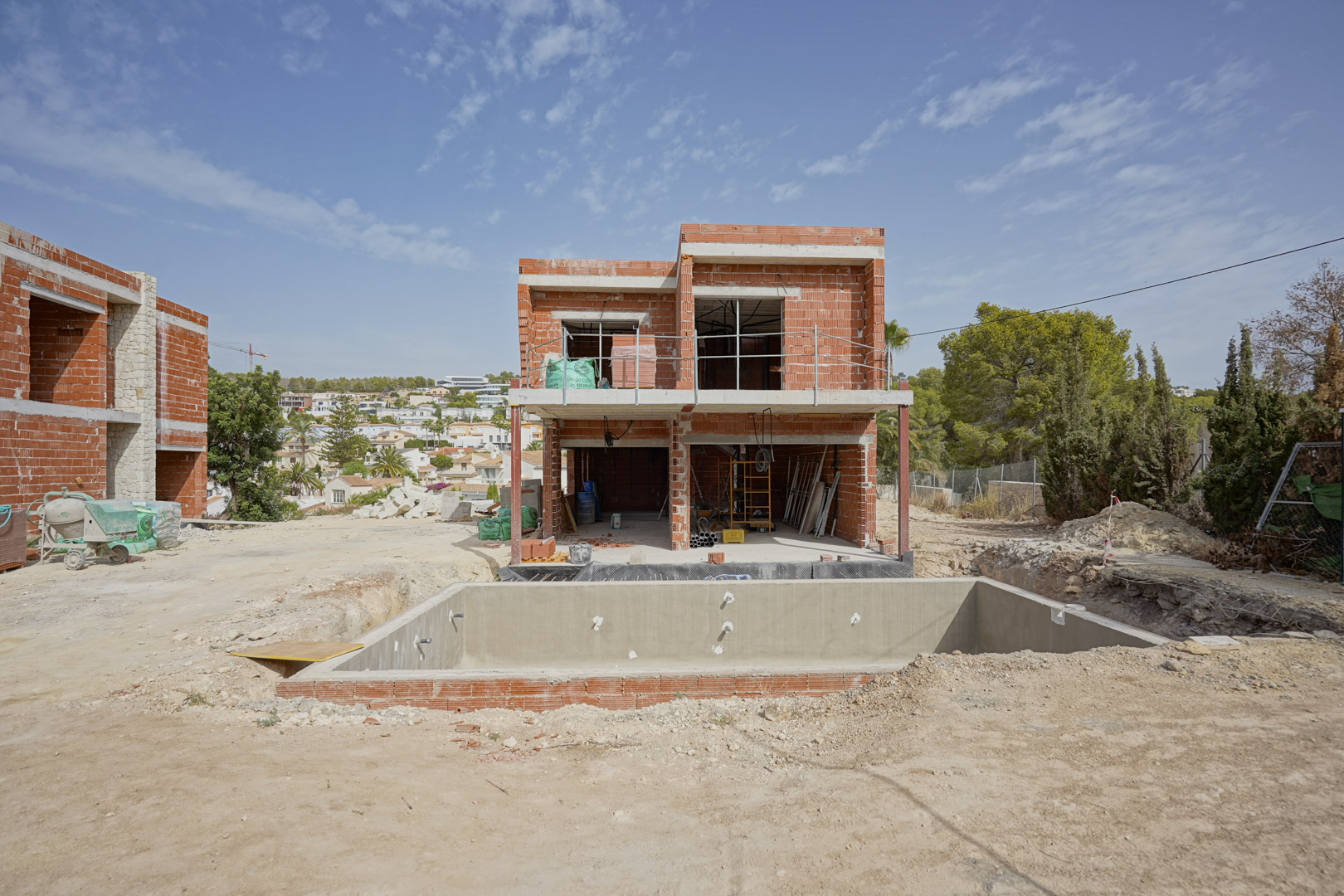 Construction progress showing the two-story brick structure and concrete pool shell. The south-facing layout and surrounding residential landscape are visible.