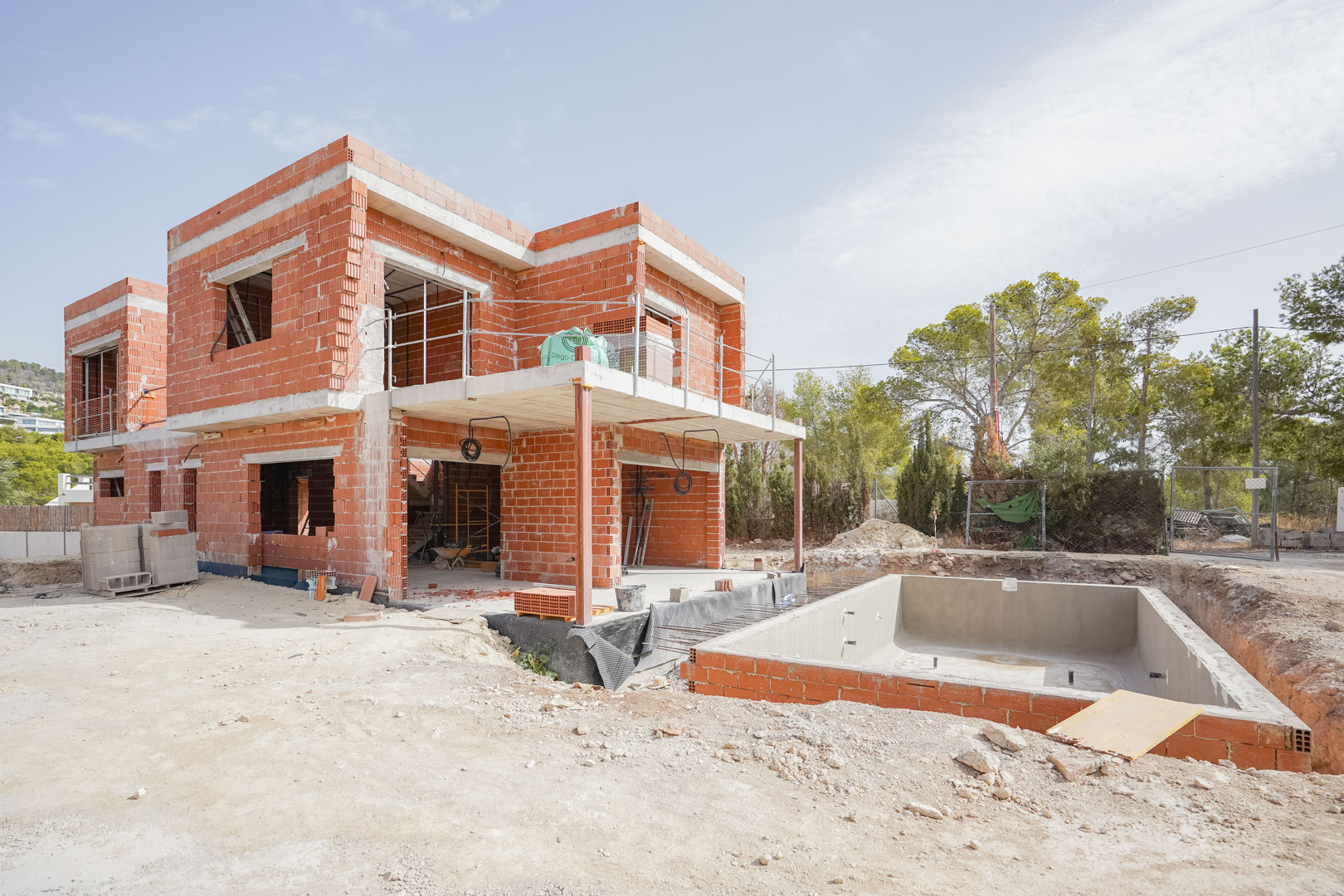 Current construction phase featuring the red brick structure, concrete floor slabs, and the excavated swimming pool shell on the private plot.