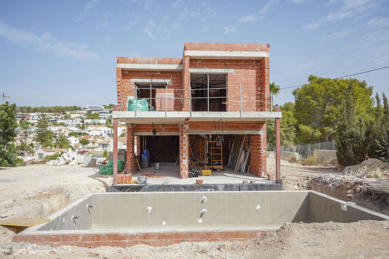 Current construction phase of the villa featuring the two-story brick shell and the concrete swimming pool basin in the foreground.