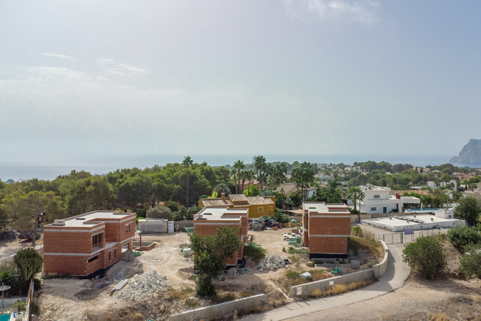 Elevated view of the three luxury villas under construction, highlighting the structural brickwork and panoramic Mediterranean Sea views with the Peñón de Ifach.