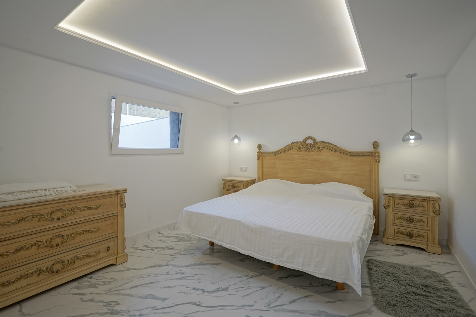 Bedroom featuring ornate classical furniture, marble-effect porcelain flooring, and a modern recessed ceiling with integrated LED perimeter lighting.