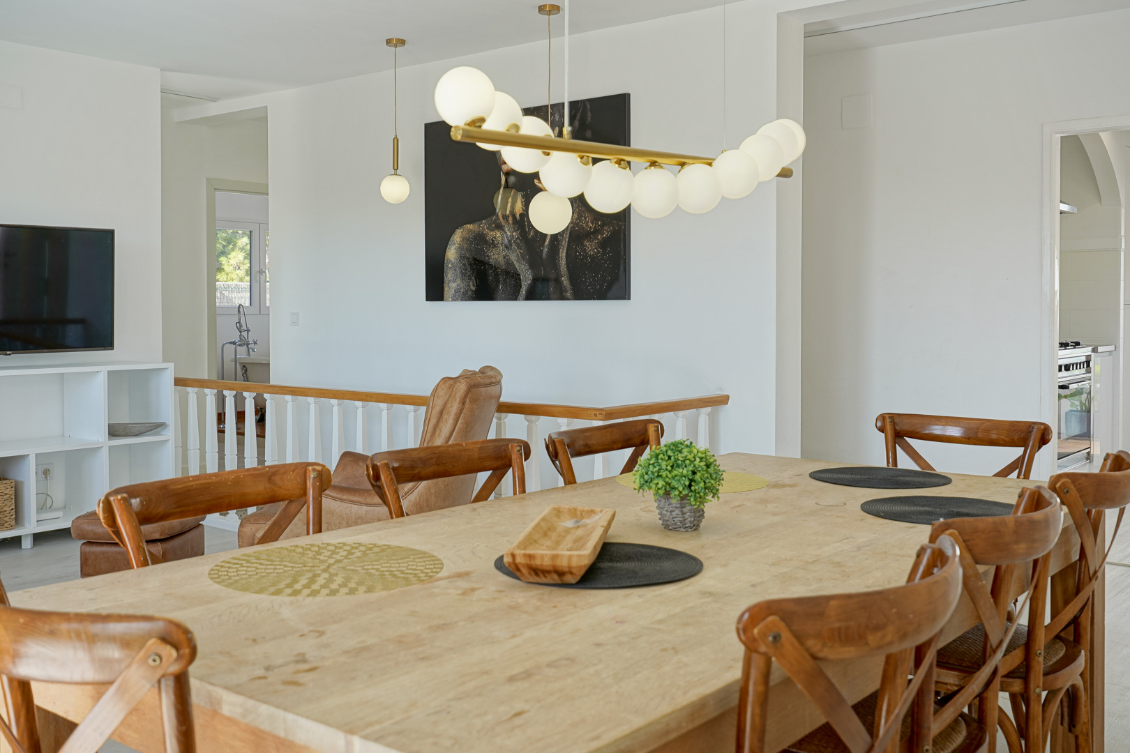 Bright dining area featuring a natural wood table and modern cross-back chairs, accented by a designer globe pendant light and open-plan layout.