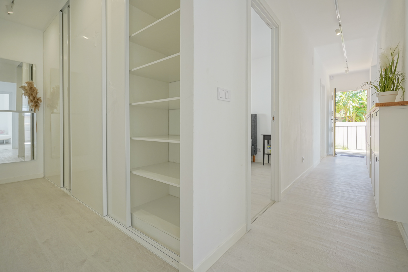 Bright hallway featuring white built-in wardrobes with sliding doors, integrated shelving, and light wood-effect flooring leading to the entrance.