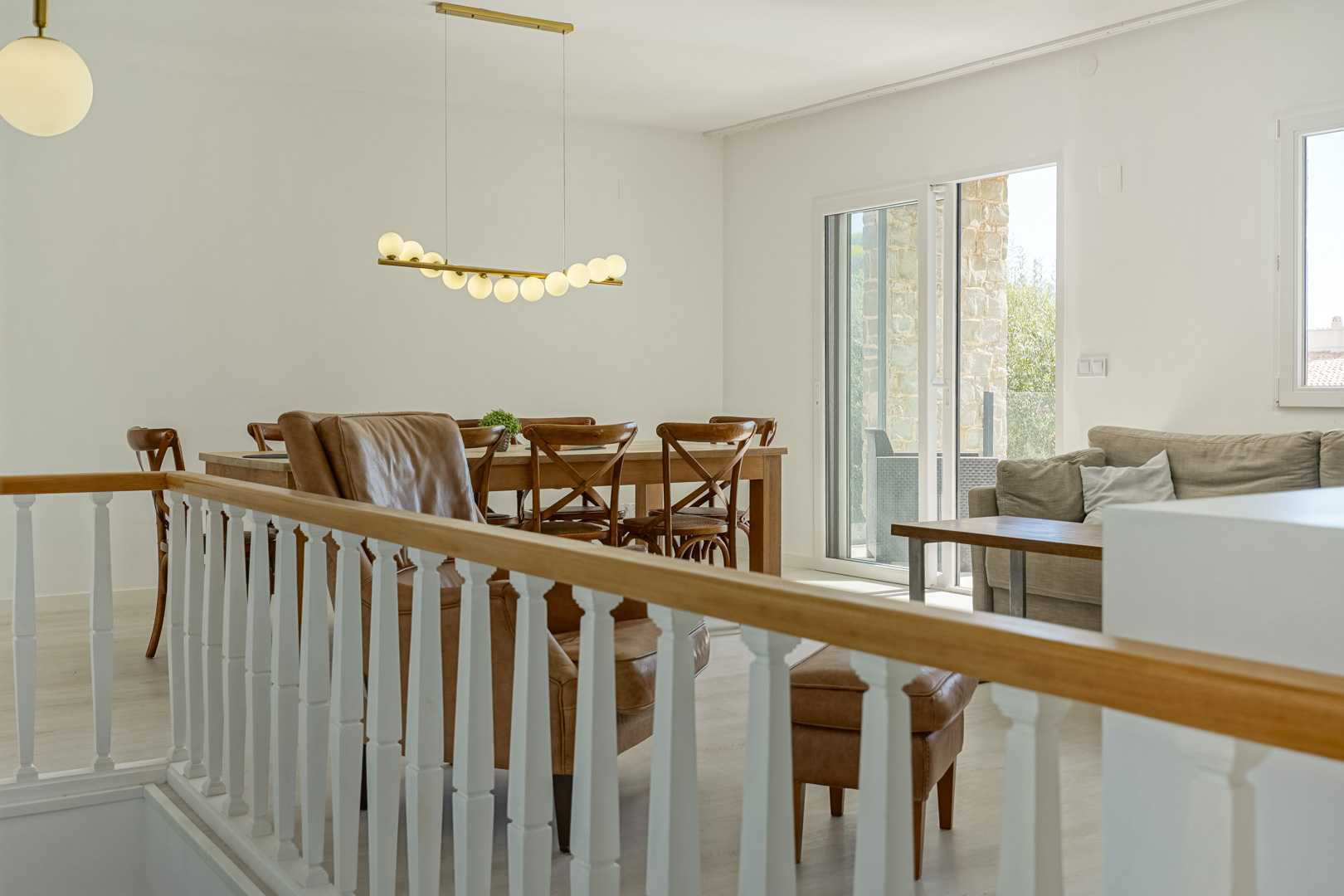 Bright living-dining area featuring a classic white balustrade, wooden dining set, designer pendant lighting, and direct access to the terrace.